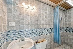 bathroom featuring toilet, walk in shower, sink, and tile walls