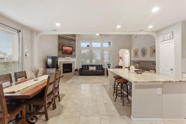 3522 Lake Lugano Cir, Katy, TX 77493 - kitchen featuring arched walkways, a fireplace, recessed lighting, light stone counters, and a center island with sink