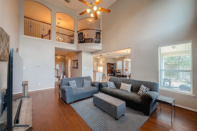 living room with ceiling fan with notable chandelier, dark wood-type flooring, and a high ceiling