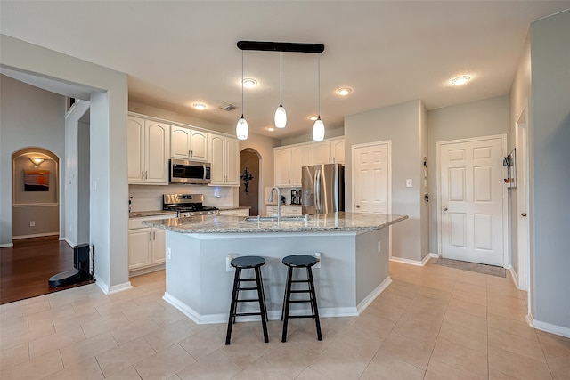 kitchen with sink, white cabinetry, stainless steel appliances, light stone counters, and a kitchen island with sink