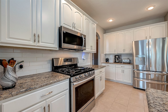 kitchen featuring decorative backsplash, light stone counters, light tile patterned floors, white cabinetry, and stainless steel appliances