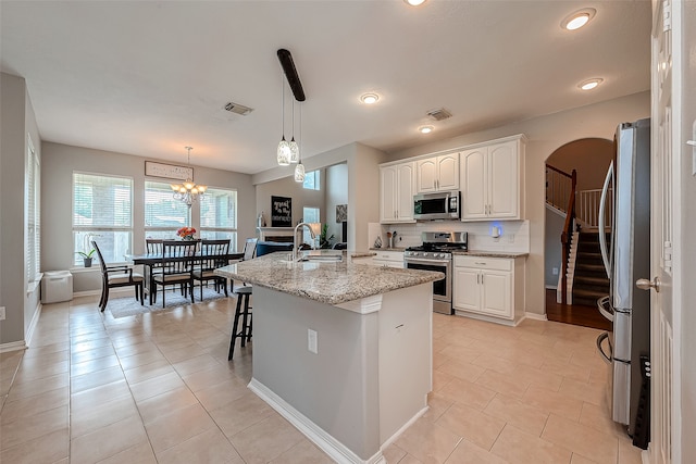 kitchen featuring white cabinets, an island with sink, appliances with stainless steel finishes, light stone countertops, and pendant lighting