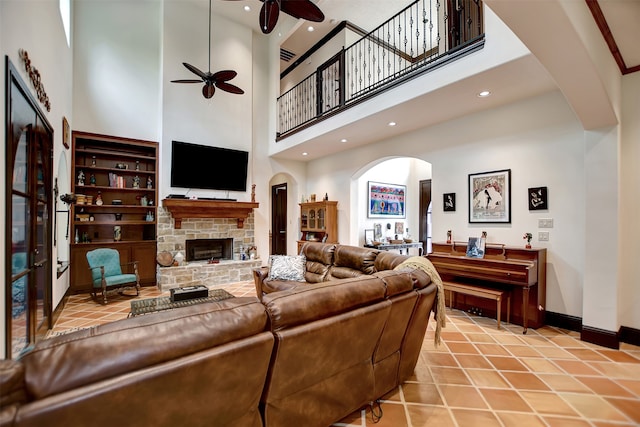 living room featuring a fireplace, light tile patterned flooring, a high ceiling, and ceiling fan