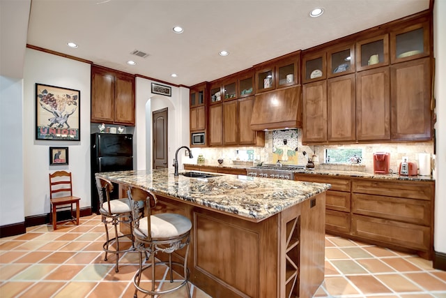 kitchen with appliances with stainless steel finishes, sink, light stone counters, ornamental molding, and a kitchen island with sink