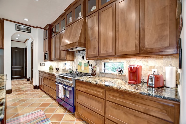 kitchen featuring high end stainless steel range oven, premium range hood, light tile patterned flooring, crown molding, and light stone counters