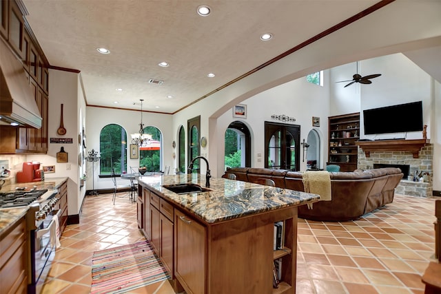 kitchen featuring an island with sink, stainless steel stove, sink, a fireplace, and decorative light fixtures