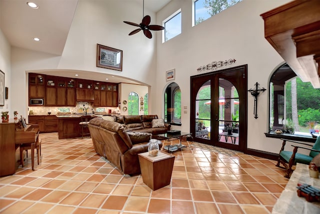 tiled living room with french doors, ceiling fan, a healthy amount of sunlight, and a towering ceiling