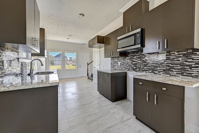 kitchen featuring decorative backsplash, dark brown cabinets, ornamental molding, sink, and a textured ceiling