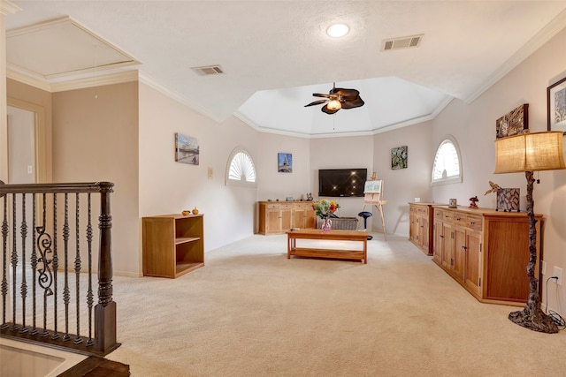 living room with ornamental molding, light colored carpet, a textured ceiling, ceiling fan, and a raised ceiling