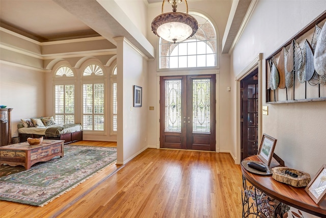 foyer entrance with ornamental molding, a towering ceiling, a healthy amount of sunlight, and light hardwood / wood-style floors