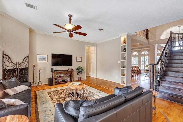 living room featuring ornate columns, ceiling fan, built in shelves, wood-type flooring, and ornamental molding