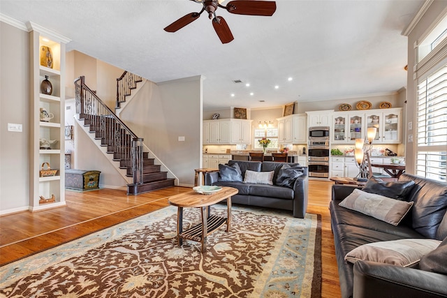 living room with ornamental molding, ceiling fan, light wood-type flooring, and built in features