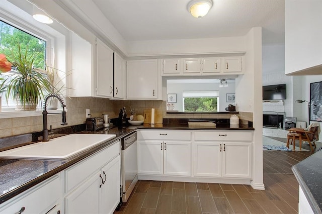 kitchen featuring stainless steel dishwasher, white cabinetry, sink, and a fireplace