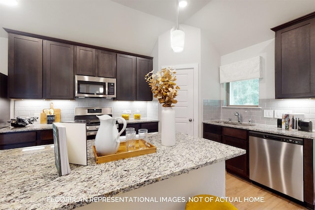 kitchen with sink, vaulted ceiling, dark brown cabinets, pendant lighting, and stainless steel appliances