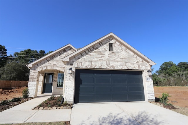 french country style house with concrete driveway, brick siding, fence, and an attached garage