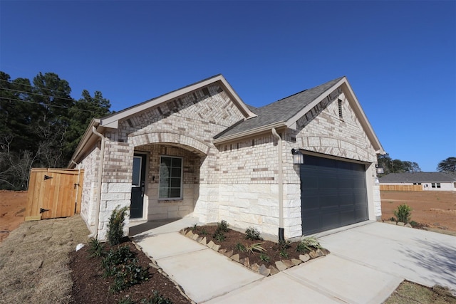 french provincial home with an attached garage, brick siding, concrete driveway, stone siding, and roof with shingles