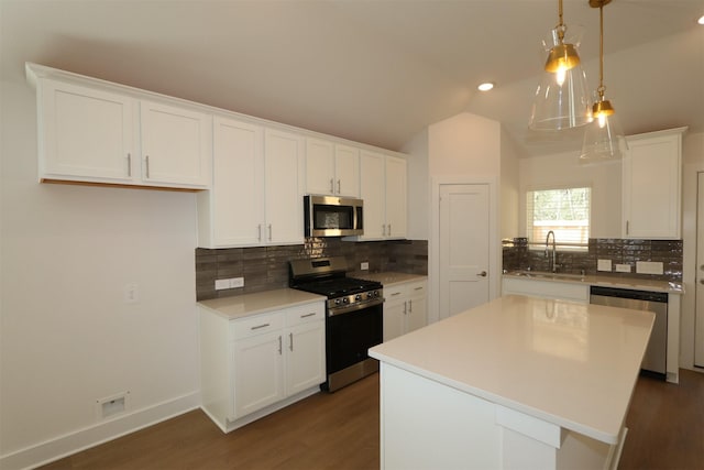 kitchen with appliances with stainless steel finishes, a center island, vaulted ceiling, white cabinetry, and a sink