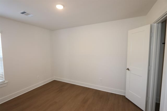 empty room with dark wood-style floors, visible vents, and baseboards