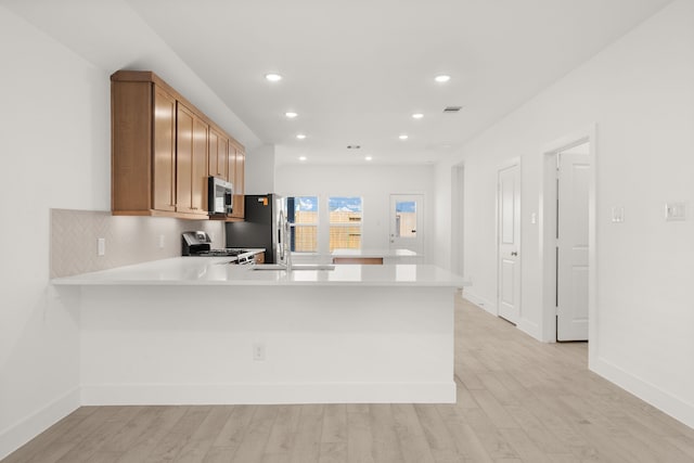 kitchen with kitchen peninsula, decorative backsplash, stainless steel appliances, and light hardwood / wood-style flooring