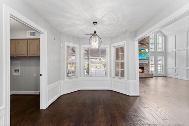 unfurnished dining area featuring a fireplace, hardwood / wood-style floors, a textured ceiling, and an inviting chandelier