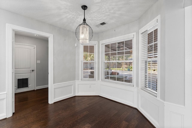 unfurnished dining area with dark hardwood / wood-style flooring, a textured ceiling, and an inviting chandelier