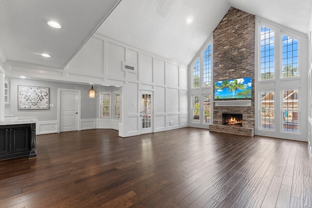 unfurnished living room with a wealth of natural light, high vaulted ceiling, dark hardwood / wood-style floors, and a brick fireplace