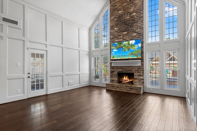 unfurnished living room featuring a fireplace, dark hardwood / wood-style floors, high vaulted ceiling, and a healthy amount of sunlight