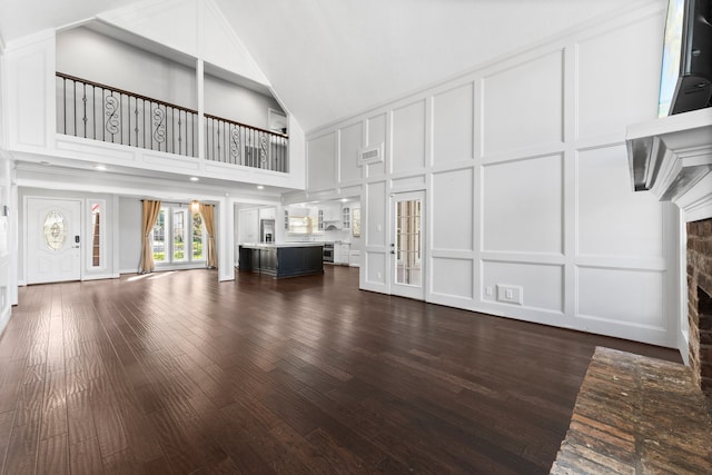 unfurnished living room with a towering ceiling, a brick fireplace, and dark wood-type flooring