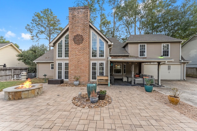 rear view of property with central AC unit, a patio area, a garage, and an outdoor fire pit