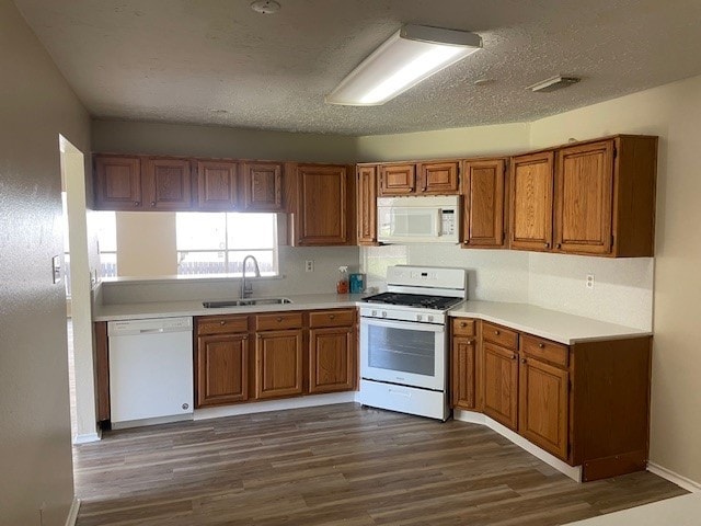 kitchen with dark wood-type flooring, a sink, brown cabinets, and white appliances