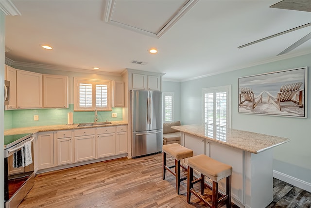 kitchen with white cabinets, stainless steel appliances, a kitchen bar, and light wood-type flooring