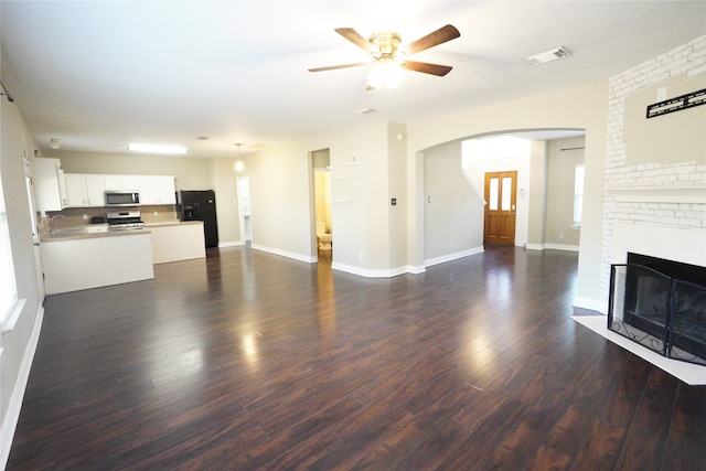 unfurnished living room with dark wood-type flooring, ceiling fan, and a brick fireplace