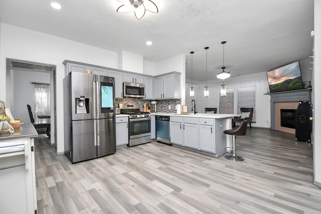 kitchen featuring appliances with stainless steel finishes, light wood-type flooring, kitchen peninsula, decorative light fixtures, and a breakfast bar