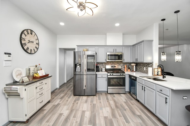 kitchen with gray cabinetry, stainless steel appliances, sink, pendant lighting, and light hardwood / wood-style floors