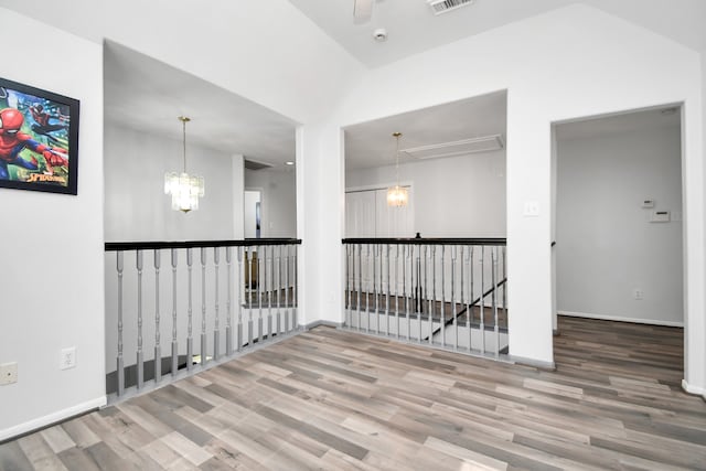 unfurnished room with wood-type flooring, vaulted ceiling, and an inviting chandelier