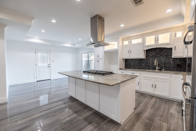 kitchen with island exhaust hood, a kitchen island, stainless steel gas cooktop, light stone countertops, and white cabinets