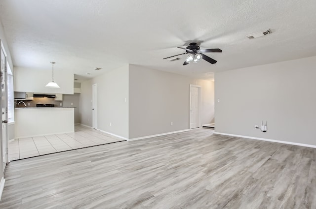 unfurnished living room with light hardwood / wood-style flooring, a textured ceiling, and ceiling fan