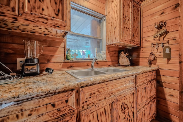 kitchen featuring sink, light stone counters, and wood walls