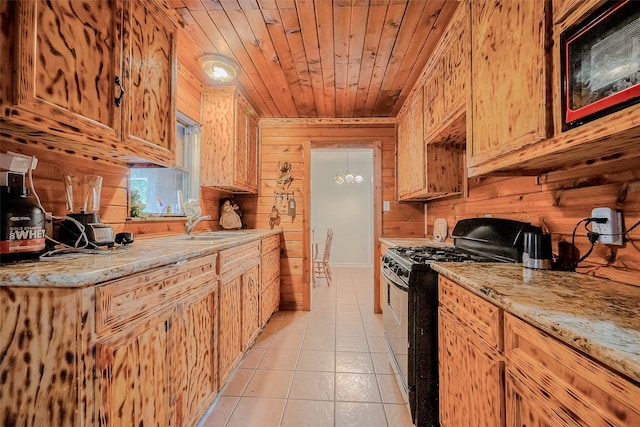 kitchen with light tile patterned floors, light stone countertops, wooden ceiling, wooden walls, and black gas range oven