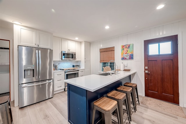 kitchen featuring appliances with stainless steel finishes, sink, a kitchen breakfast bar, white cabinets, and light hardwood / wood-style flooring