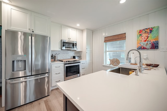 kitchen with appliances with stainless steel finishes, sink, light wood-type flooring, backsplash, and white cabinetry