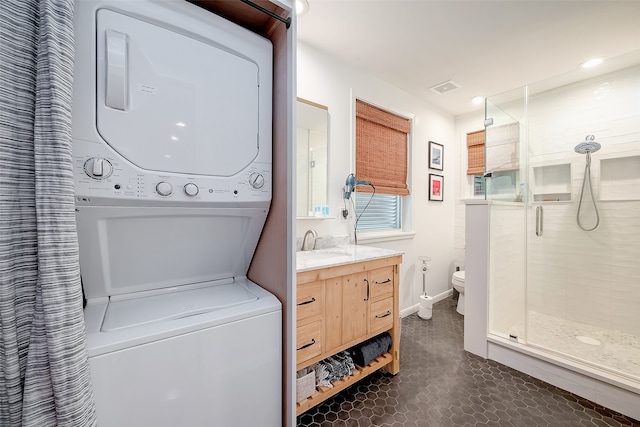 washroom featuring stacked washer / drying machine, sink, and dark tile patterned floors