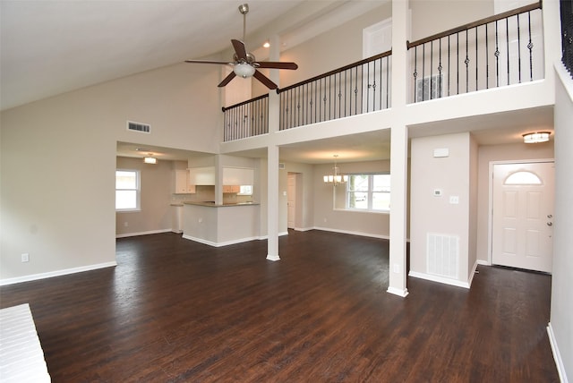 unfurnished living room with ceiling fan with notable chandelier, a towering ceiling, dark hardwood / wood-style floors, and plenty of natural light