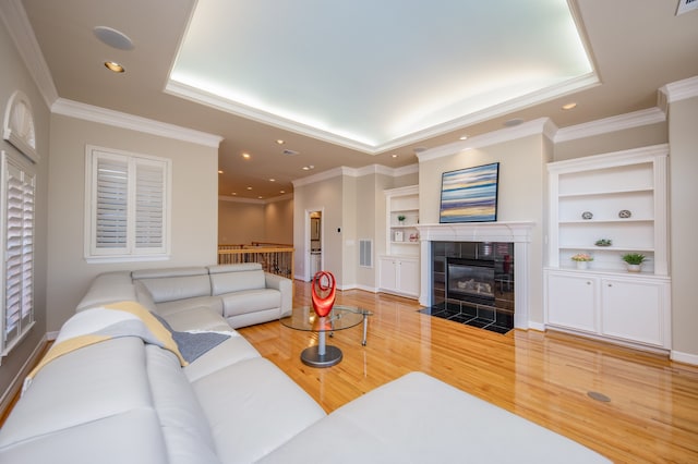 living room with ornamental molding, hardwood / wood-style floors, a tiled fireplace, and built in features