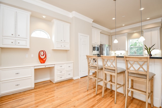 kitchen featuring built in desk, white cabinets, pendant lighting, appliances with stainless steel finishes, and light hardwood / wood-style floors