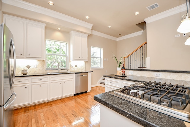 kitchen with appliances with stainless steel finishes, sink, pendant lighting, white cabinets, and light hardwood / wood-style flooring