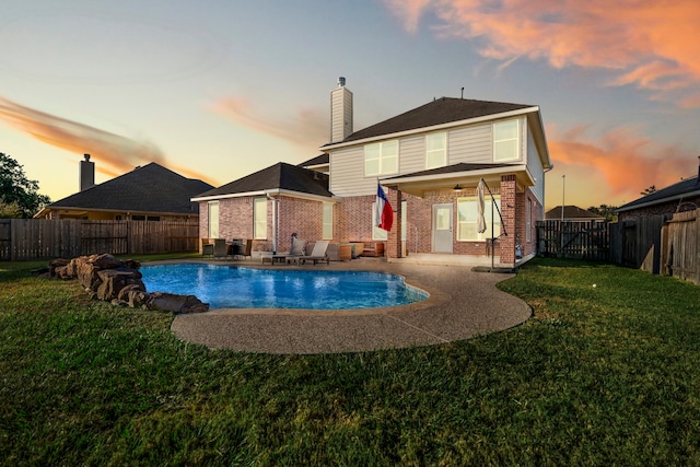 back house at dusk featuring a patio, a lawn, and a fenced in pool