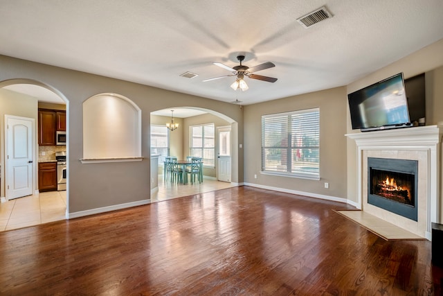 unfurnished living room with a textured ceiling, light hardwood / wood-style flooring, a tile fireplace, and ceiling fan with notable chandelier