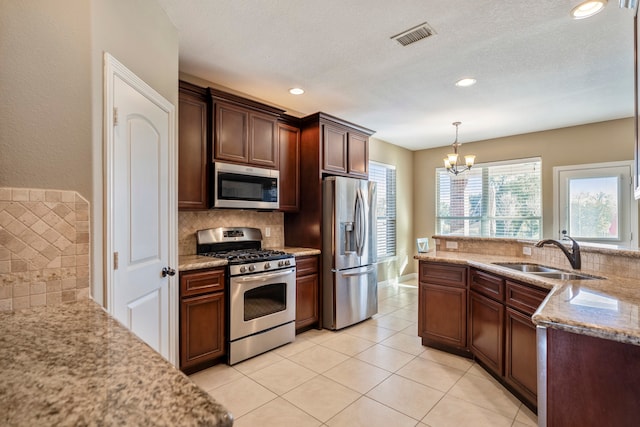 kitchen with sink, stainless steel appliances, decorative light fixtures, light stone counters, and a notable chandelier