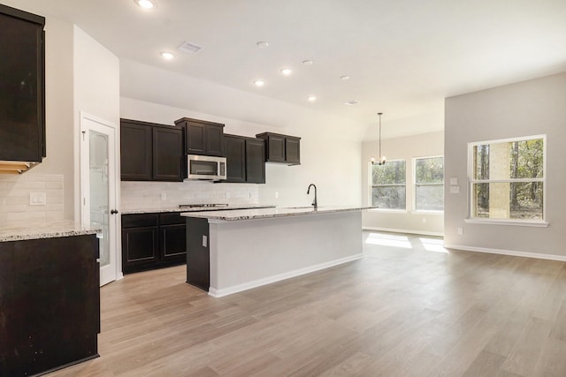 kitchen featuring decorative light fixtures, a kitchen island with sink, appliances with stainless steel finishes, and light hardwood / wood-style flooring